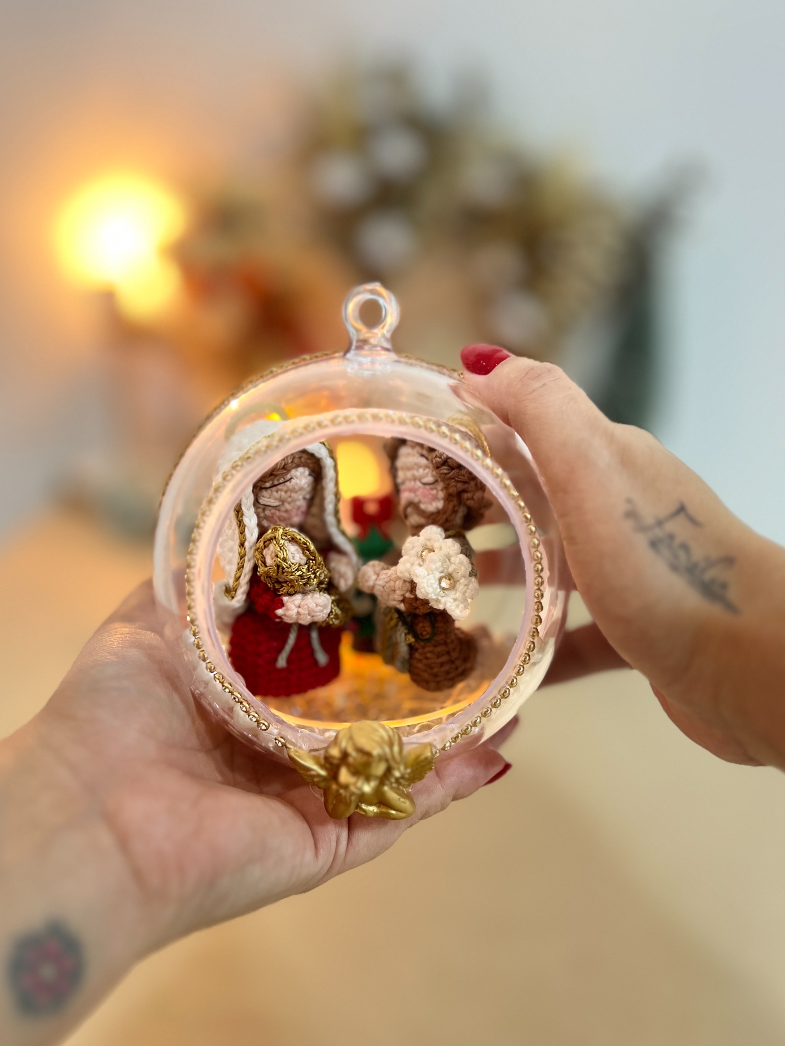 Mãos da Paula segurando a esfera da Sagrada Família em crochê
