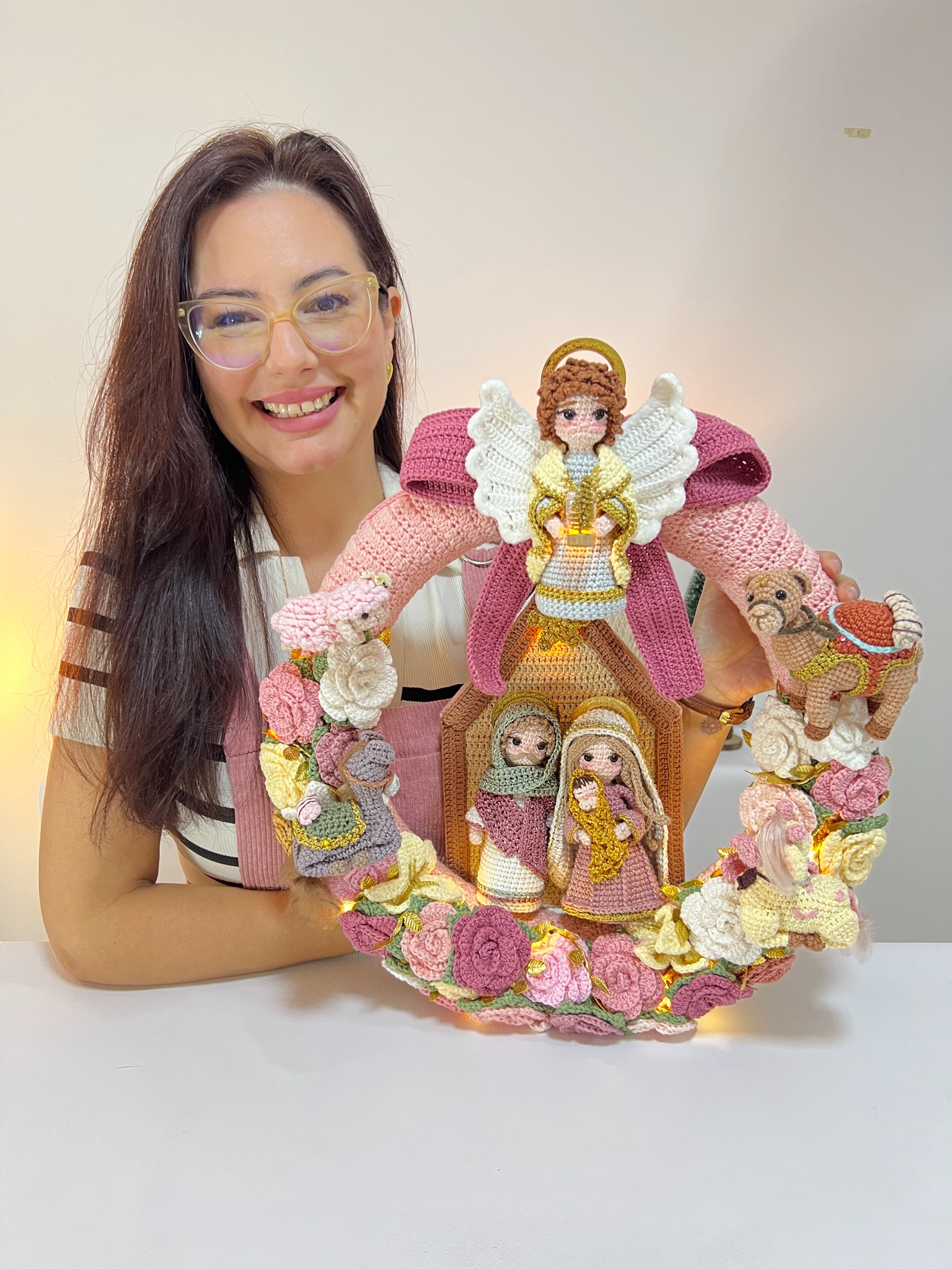 Paula com sua guirlanda rosa em crochê, com a Sagrada Família, flores, personagens e luzes